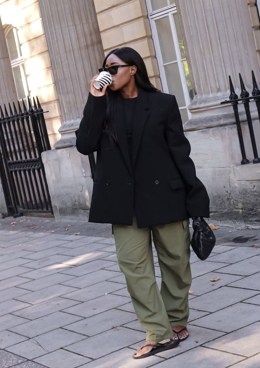 A pro stylist-inspired outfit featuring an oversized black structured blazer layered over a fitted black top with olive green wide-leg trousers.