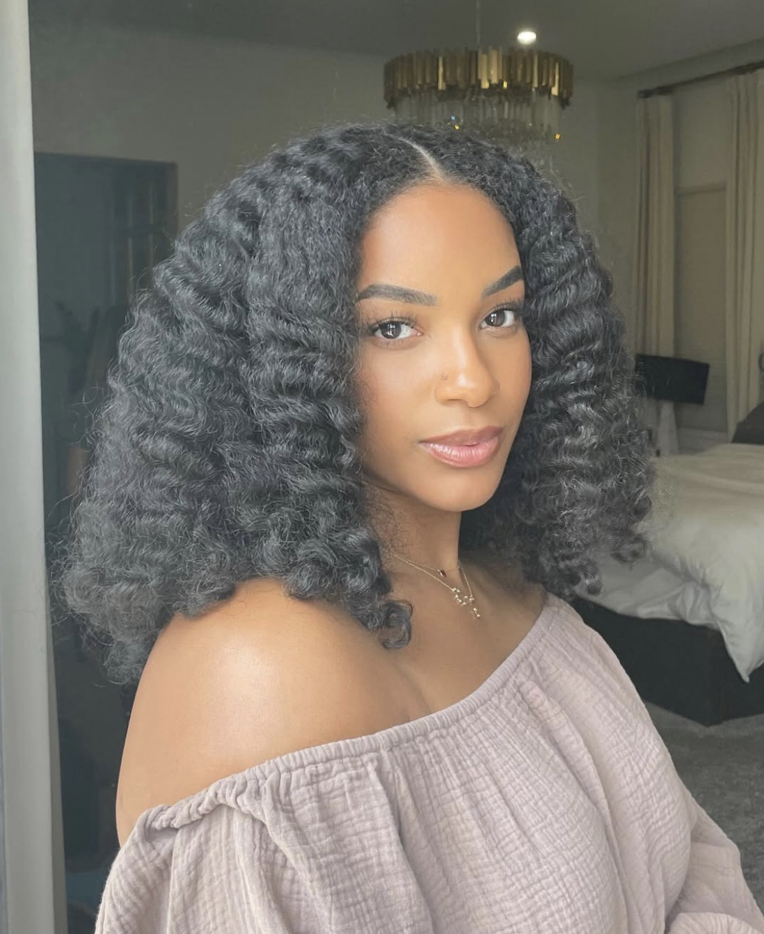 Kayla Bishop with a voluminous textured braid-out and a middle part, wearing a mauve off-the-shoulder top to showcase how volume at the ends balances a heart face shape.