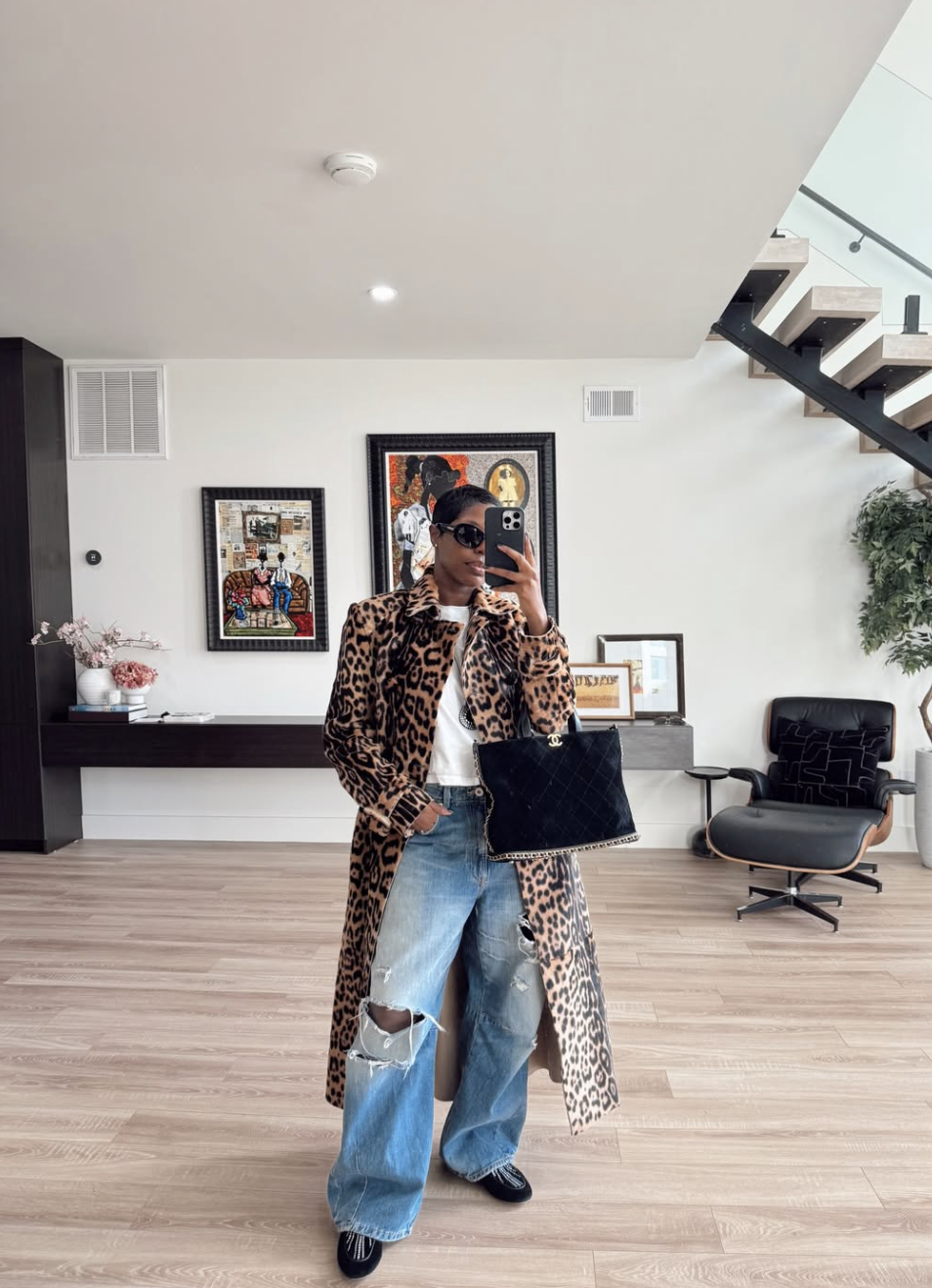 A woman wearing a leopard print jacket over a white t-shirt and light wash baggy jeans, holding a black quilted handbag.