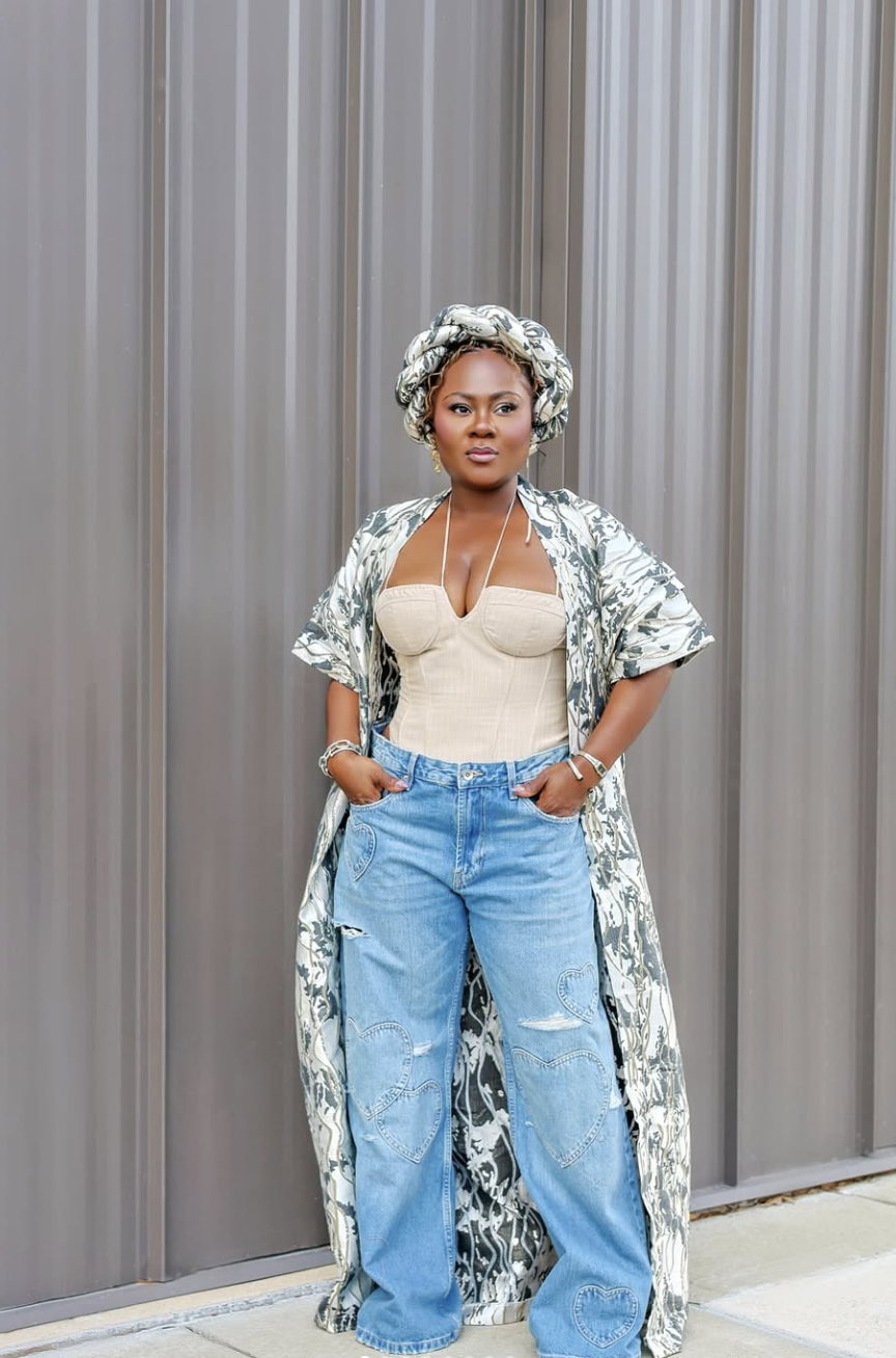 A woman wearing light wash wide-leg distressed jeans with a beige corset top and a matching green and white patterned duster and headwrap.