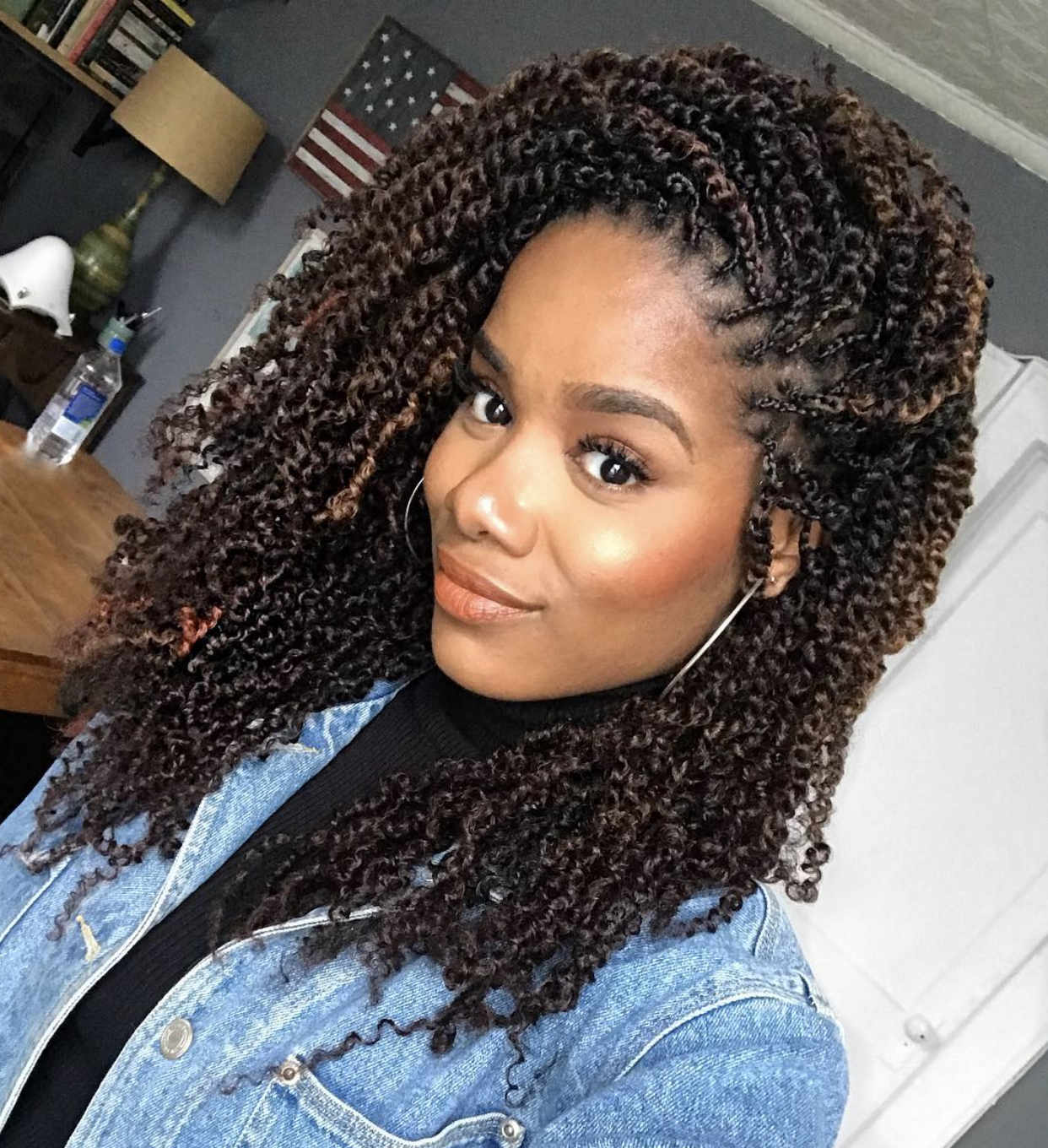 A woman with shoulder-length, curly passion twists in a dark brown shade, wearing a denim jacket over a black turtleneck and showcasing how the volume softens a diamond face shape.