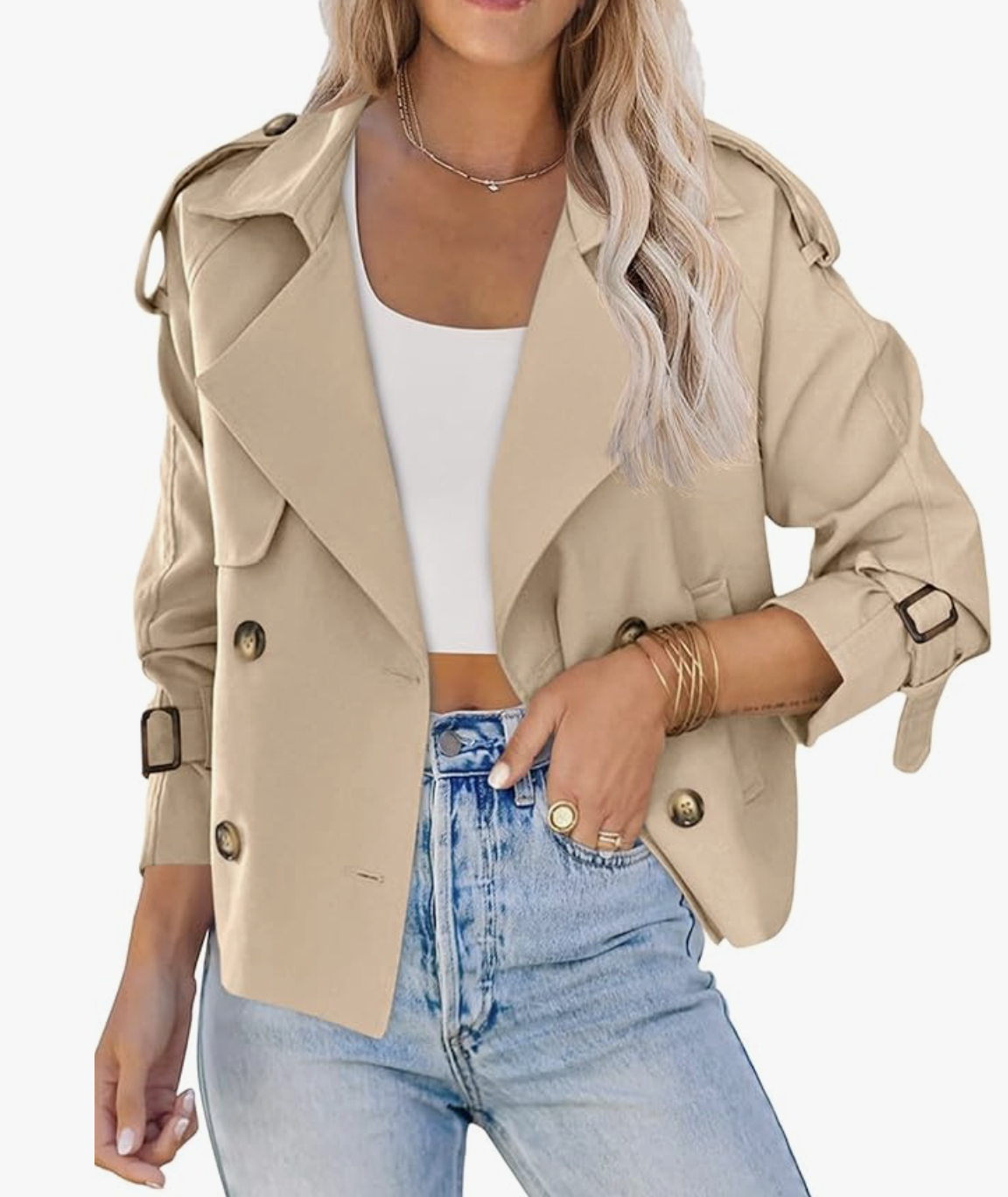 A woman wearing a khaki double-breasted trench coat over a white top and light-wash jeans, featuring gold button details and belted cuffs—a perfect transitional layer for a hybrid work capsule wardrobe.