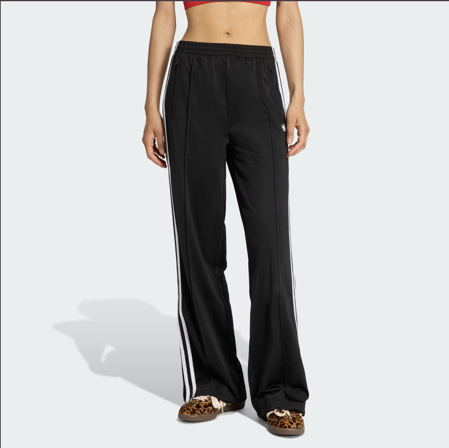 A pair of black Adidas Firebird Loose Track Pants with classic white side stripes, demonstrating a voluminous wide-leg silhouette that can be styled as professional trousers.