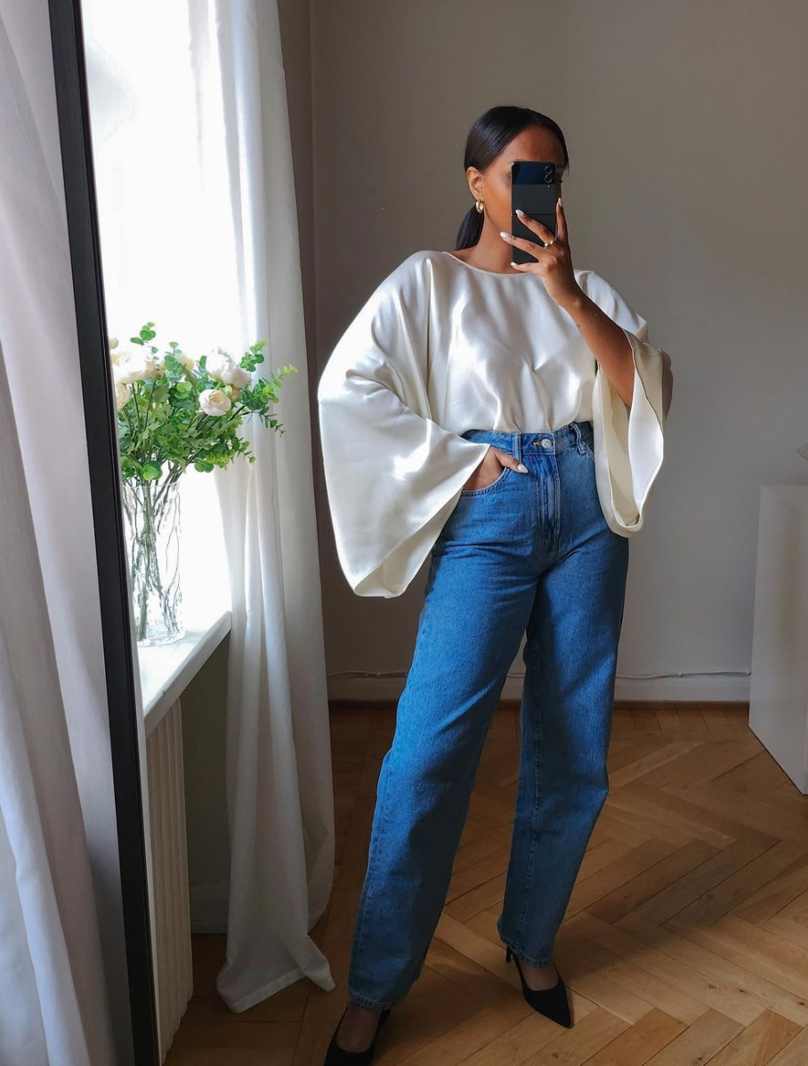 A woman (Sofia Richie) wearing a minimalist white top tucked into high-waisted blue jeans, demonstrating the Quiet Money aesthetic through elevated basics.