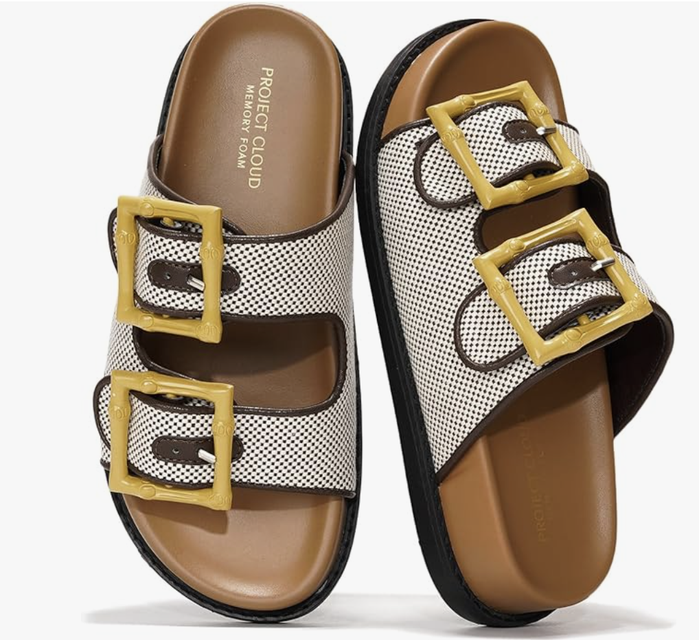 A close-up of a pair of brown genuine leather slide sandals featuring two adjustable straps with large gold buckles and a comfortable contoured footbed, styled for a 50 plus spring capsule wardrobe.
