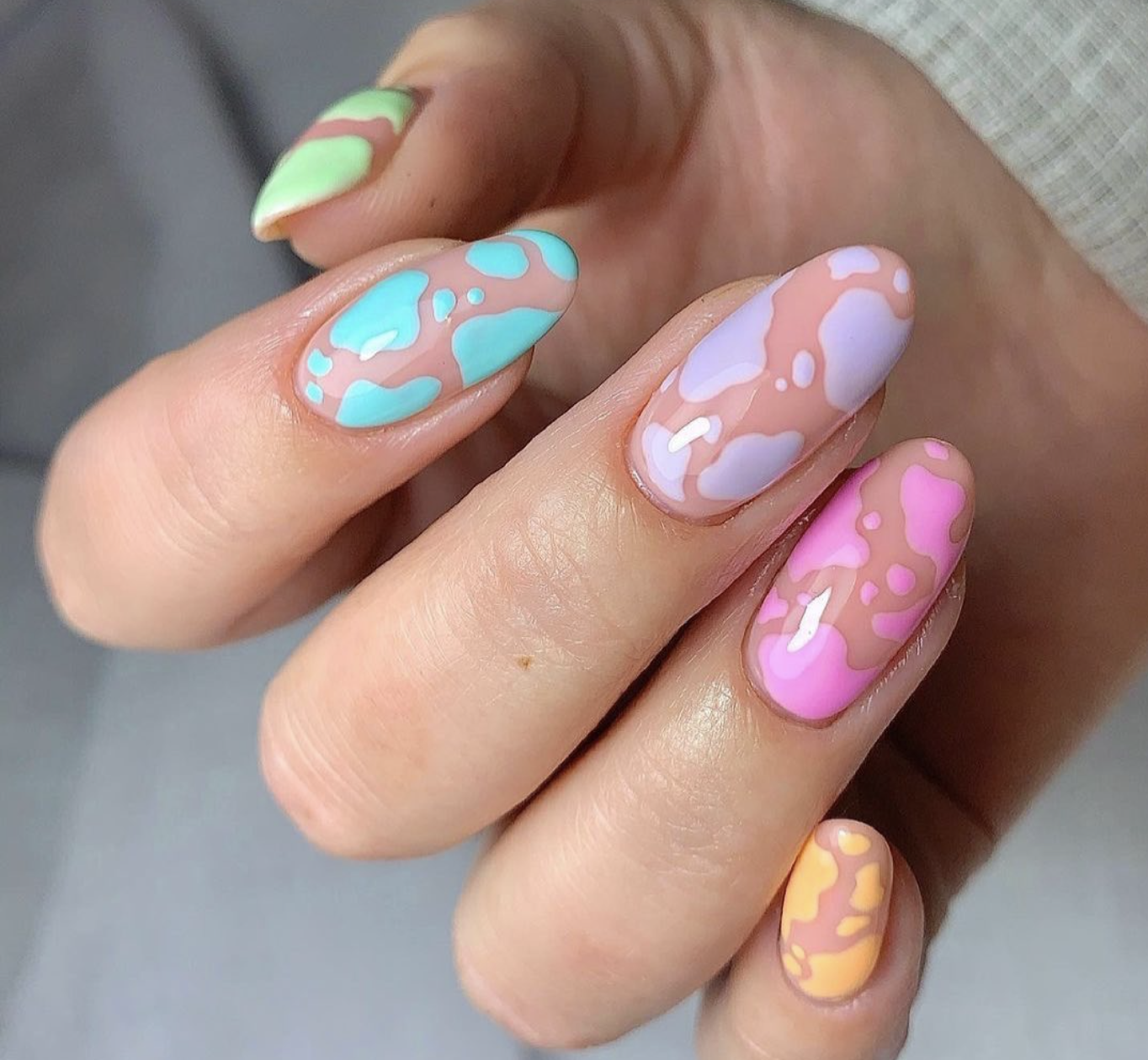 Long almond-shaped nails featuring a colorful cow print pattern in pastel shades of mint green, lavender, pink, and peach.