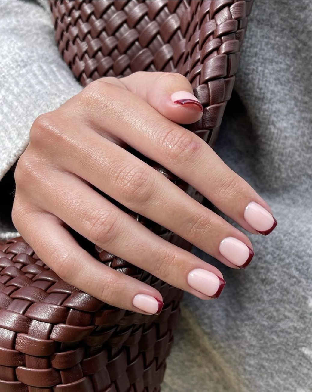 Close-up of short squoval nails with a deep black cherry burgundy micro French tip over a sheer nude pink base.