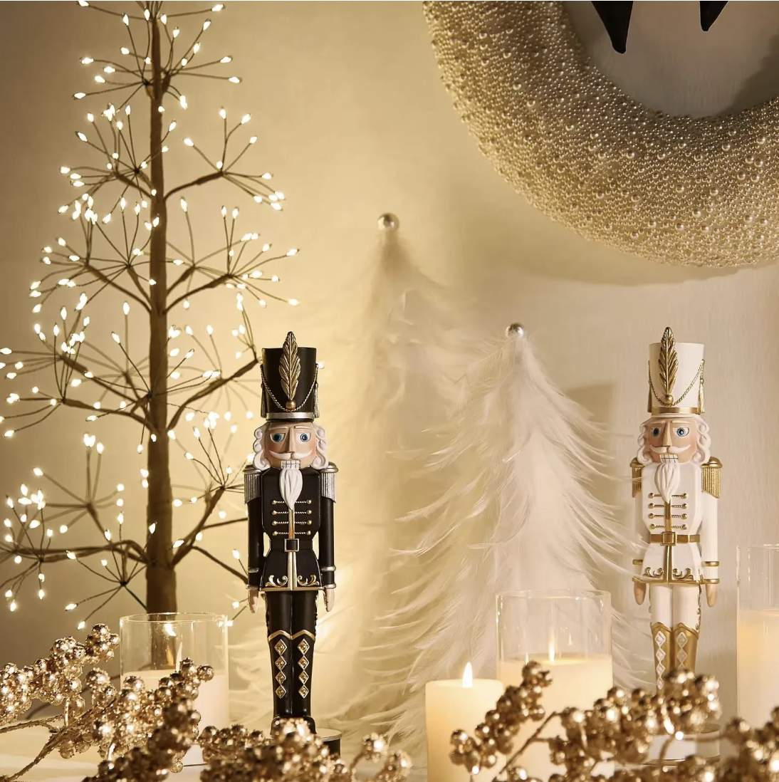 Black and white nutcracker figures on a mantel with a lit twig tree, white feather trees, gold berry sprigs and pillar candles.