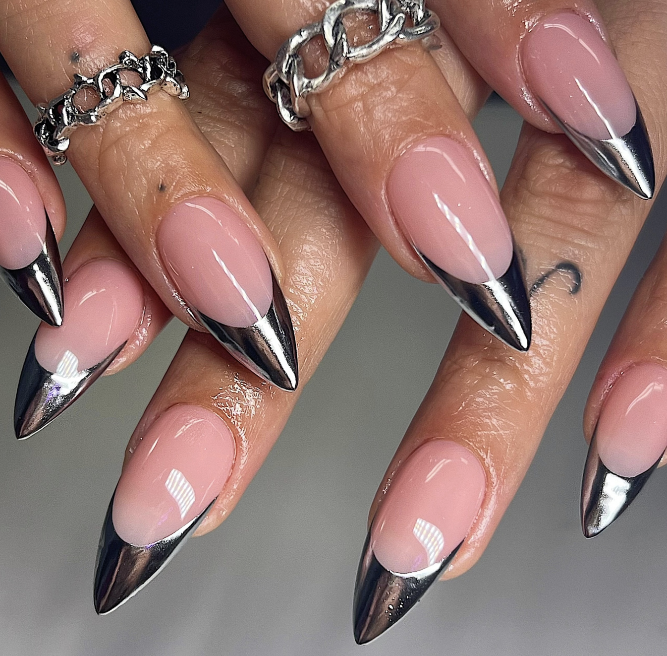 Long almond-shaped nails with a high-shine silver chrome mirror finish on the French tips over a translucent pink base.
