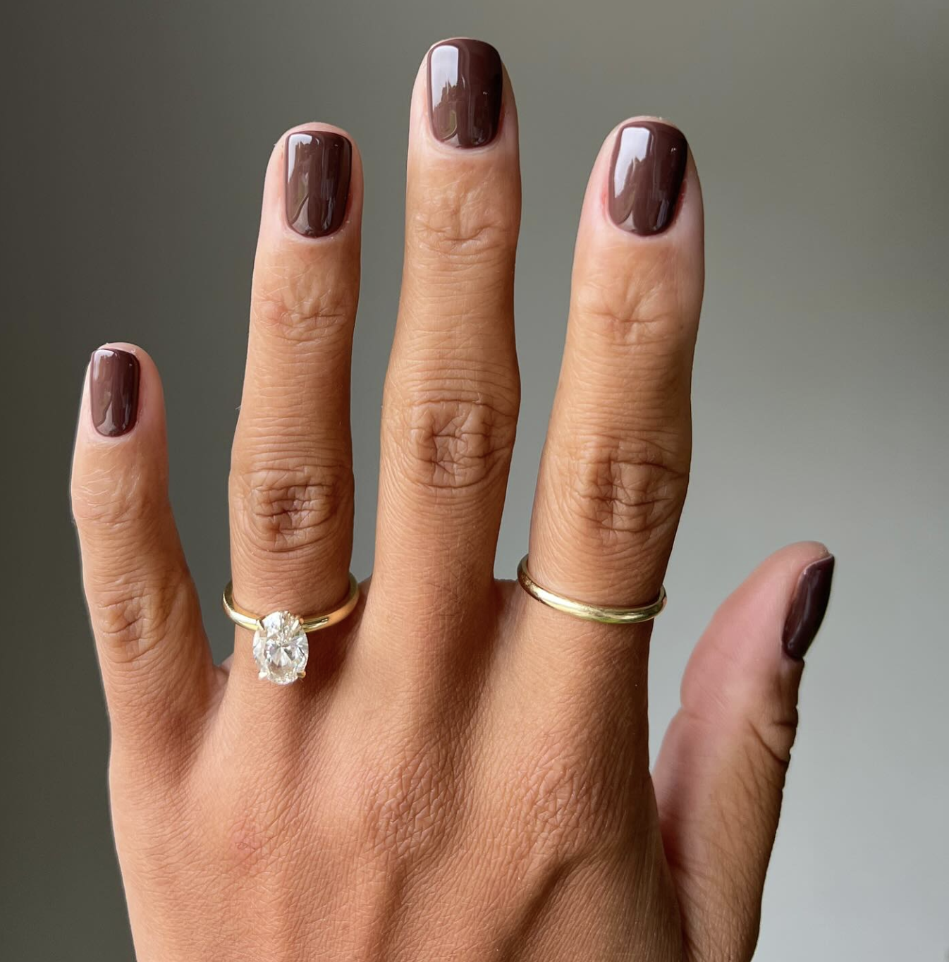 Close-up of short nails featuring a glossy sheer cocoa brown jelly manicure with gold rings.