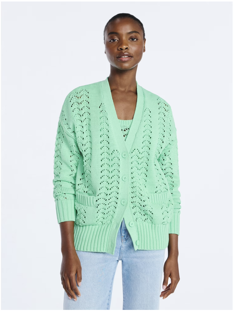 A woman wearing a mint green V-neck button-down cardigan with an intricate crochet-knit pattern, paired with light-wash denim jeans.