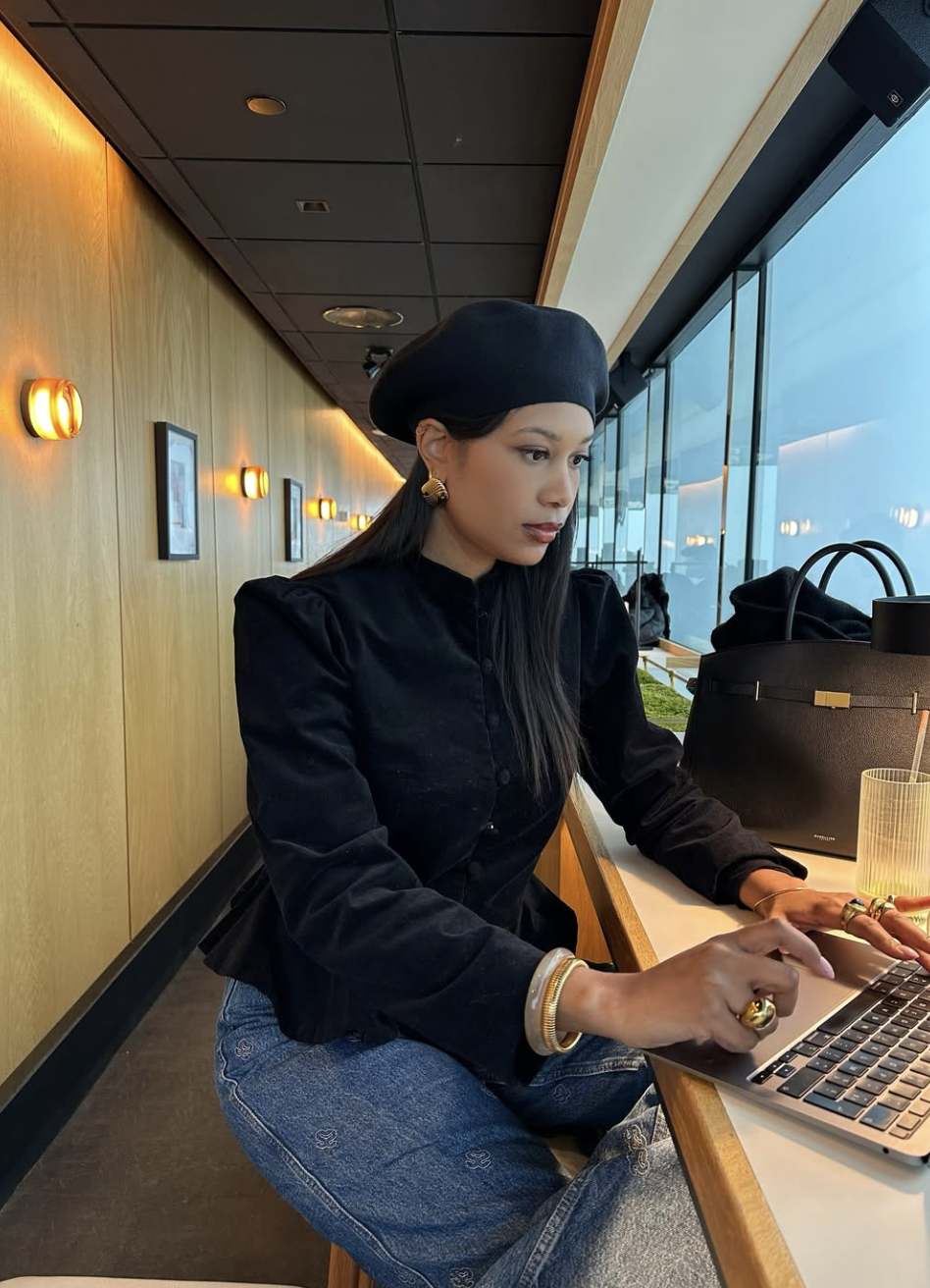 Close up of a dark poetcore outfit featuring a structured black button-down shirt, blue denim, and a gold-accented bracelet, styled with a classic leather satchel bag.