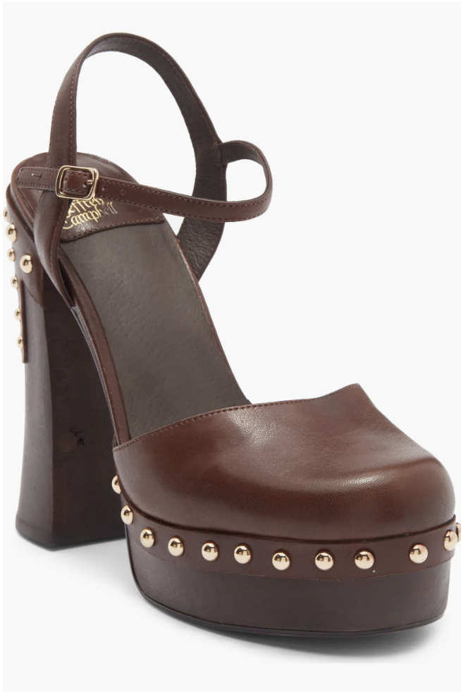 A close-up shot of a luxury dark brown leather platform clog shoe featuring a chunky high wooden heel and polished gold stud detailing along the sole.