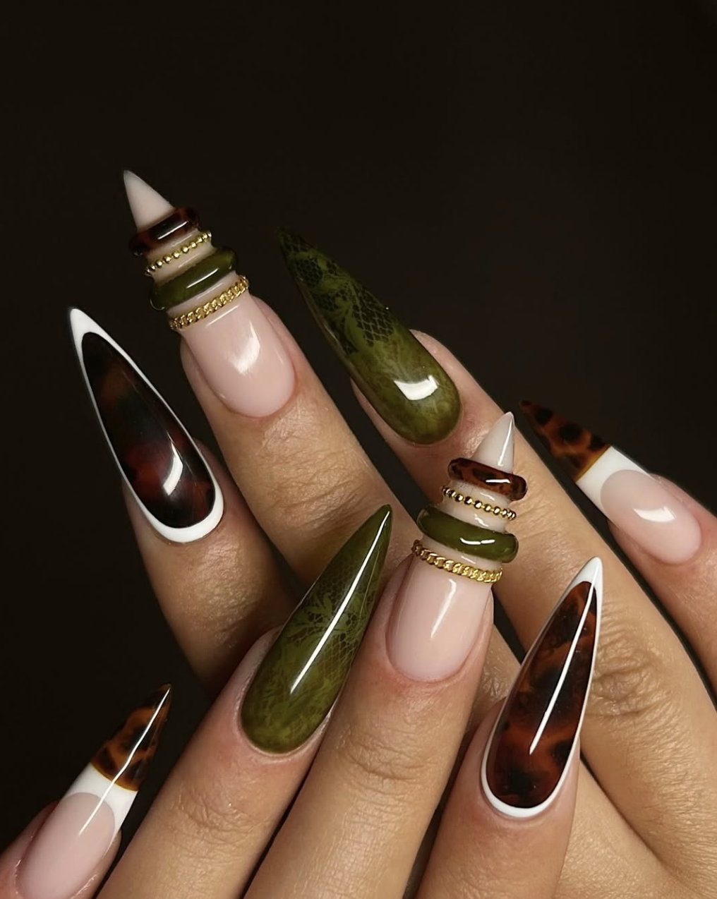 Pointed almond nails featuring a mix of deep moss green snakeskin texture, tortoise shell patterns, and thick 3D gold bangle bands.