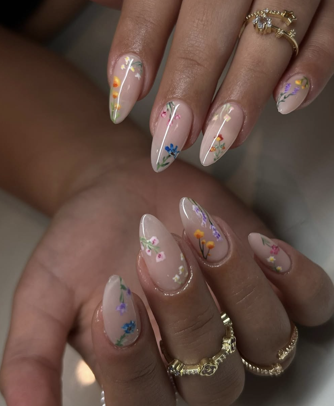 Almond-shaped sheer nude nails with tiny, delicate hand-painted white daisies and soft yellow centers.