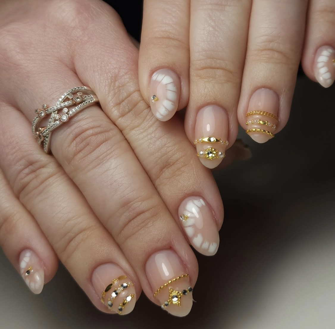 Milky white almond nails with 3D gold bangle bands, tiny gold studs, and soft white cloud accents.