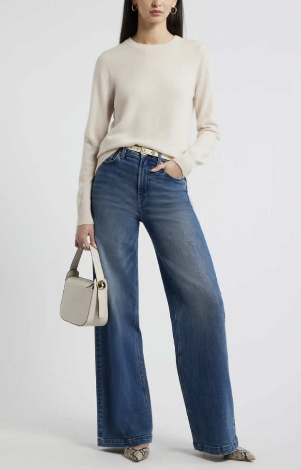 Woman wearing a cream crewneck sweater tucked into wide-leg jeans with a cream shoulder bag and snakeskin pointed flats.