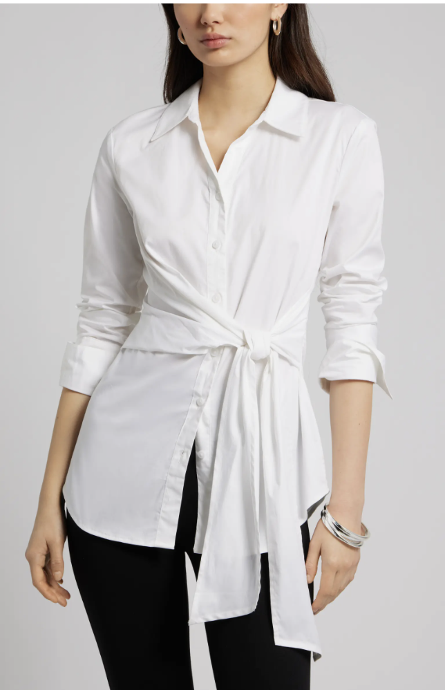 A woman wearing a white cotton poplin button-up shirt featuring a unique wrap-around waist tie detail and long sleeves, styled with black pants.