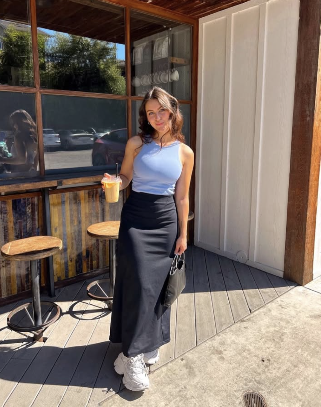 Woman standing outdoors on a wooden deck wearing chunky white court sneakers with a black maxi skirt.