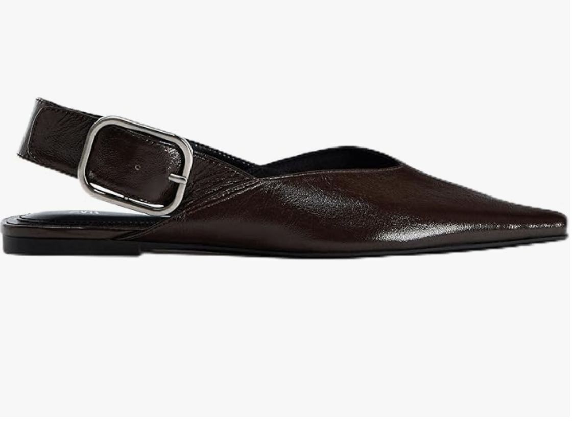 A pair of black leather pointed-toe flat mules with a large silver buckle strap, a sophisticated shoe option to pair with white straight-leg jeans.