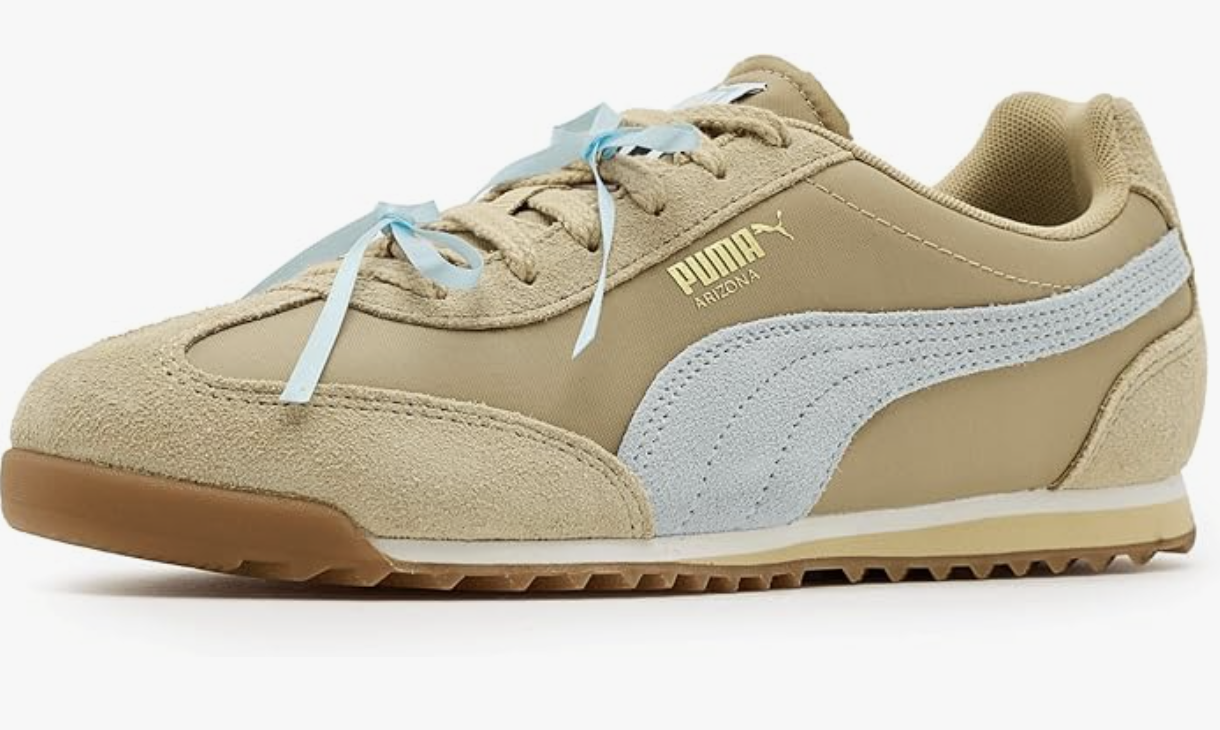 A pair of tan suede Puma Arizona Bow sneakers with light blue ribbon laces and a gum sole on a white background.