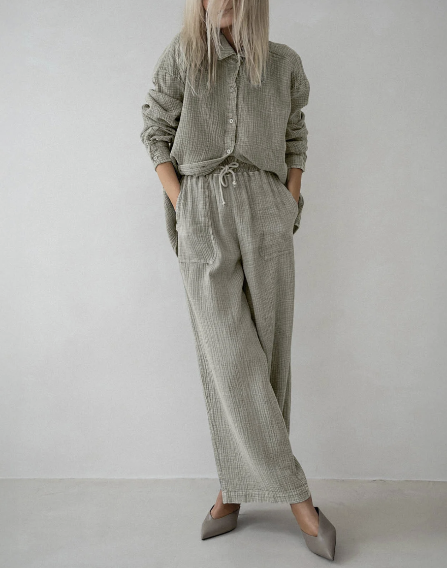 A person wearing an oversized sage green linen button-down shirt and matching wide-leg trousers with grey pointed-toe kitten heels.
