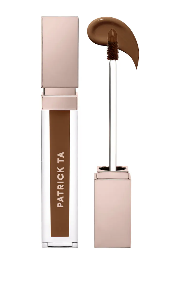 A tube of Patrick Ta Major Skin Soft Blur Brightening Concealer in a deep brown shade with the applicator wand pulled out to show a swatch of the liquid formula.