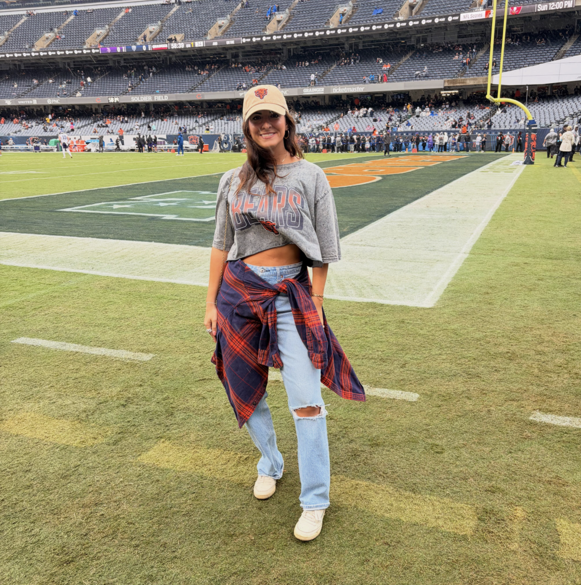 Woman at a Chicago Bears game wearing a gray Bears graphic tee, ripped light-wash jeans, plaid shirt and white sneakers.