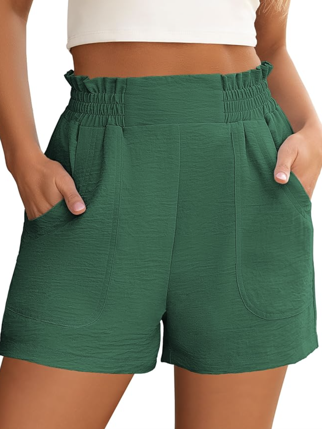 A woman wearing sage green textured pleated shorts with a high-waist tie, designed to add fullness and shape to skinny legs.