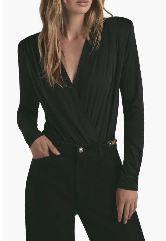 Close-up of a woman wearing high-waisted black cigarette jeans with a metallic button, styled with a black long-sleeve wrap top.
