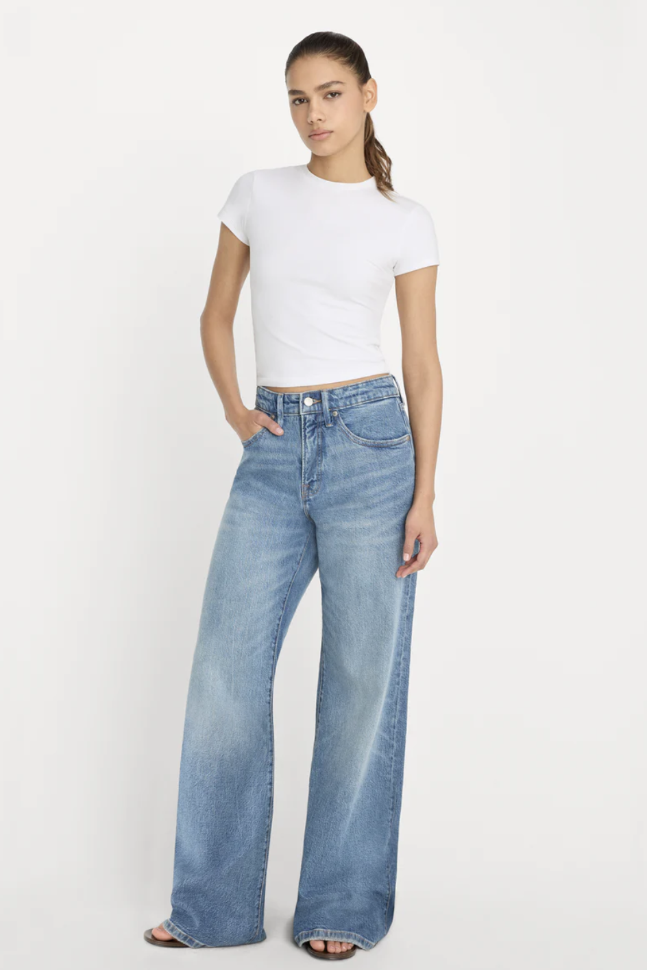 ront view of a person wearing Good American wide-leg blue jeans styled with flat black leather flip flop sandals.