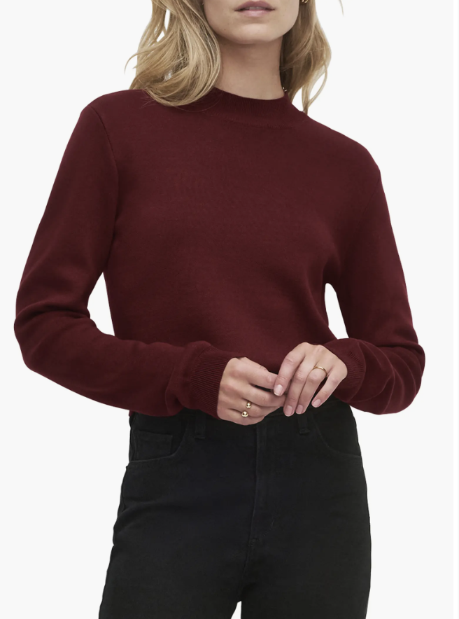 Woman wearing a fitted burgundy mock-neck sweater with black jeans.