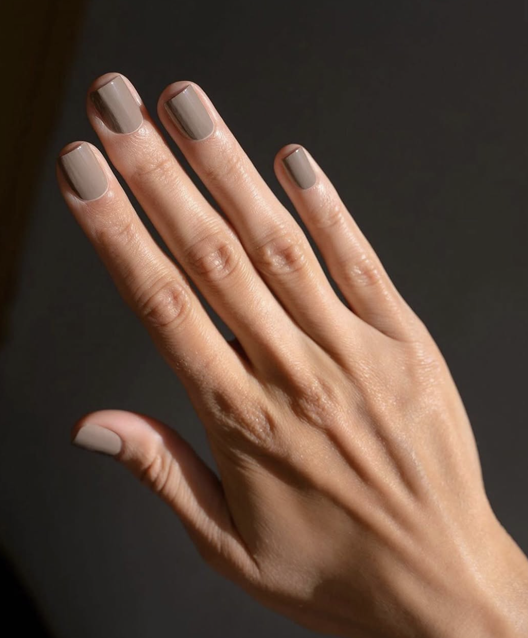 Close-up of short squoval nails painted in a glossy mushroom taupe nail polish.