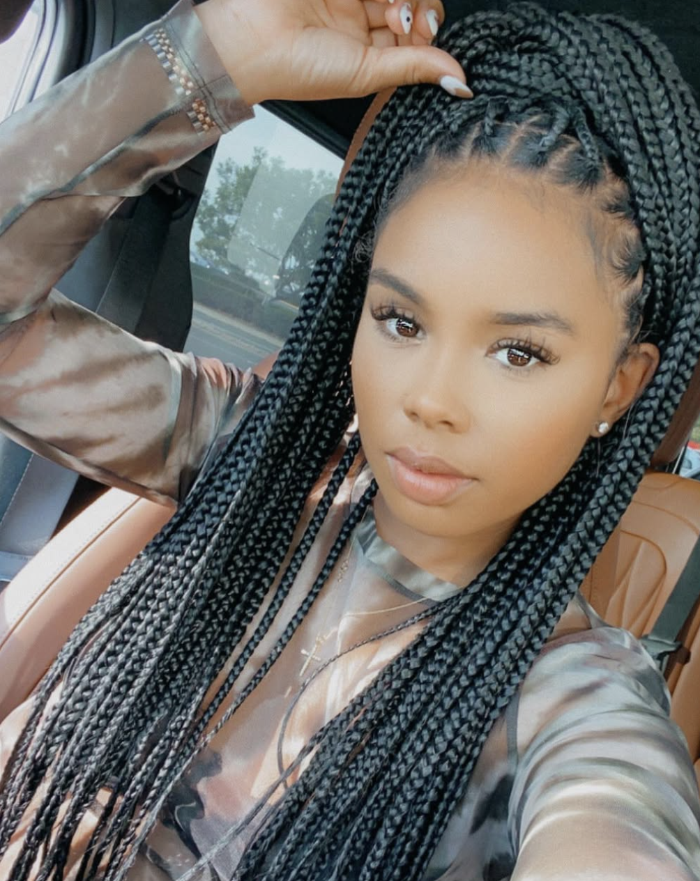 A woman with a square face shape wearing long box braids with a side part and warm brown color at the tips, illustrating how length and asymmetry frame a strong jawline.
