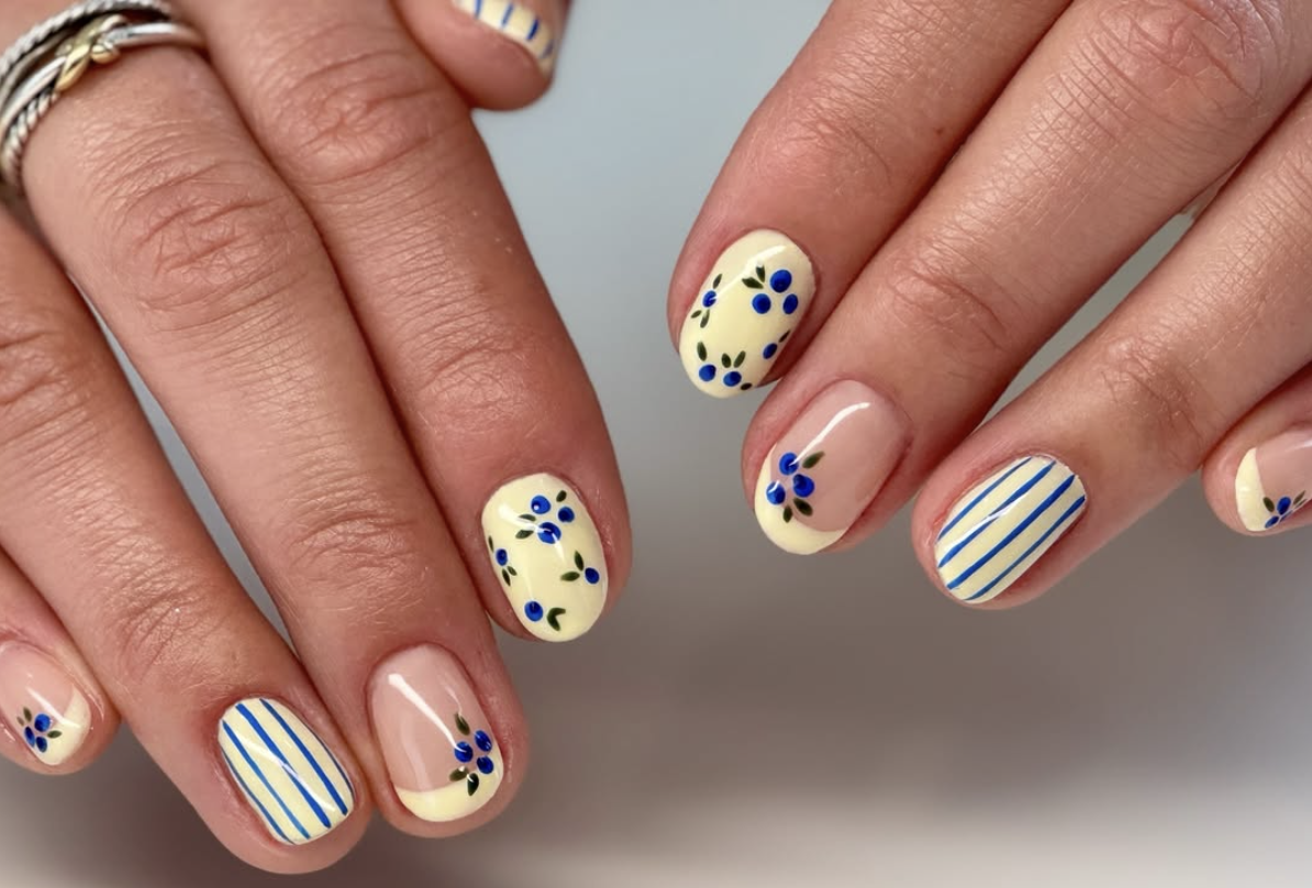 A high-feminine spring manicure by @color.and.cure featuring butter yellow almond nails with intricate blue floral patterns and dainty blue and white vertical stripes.