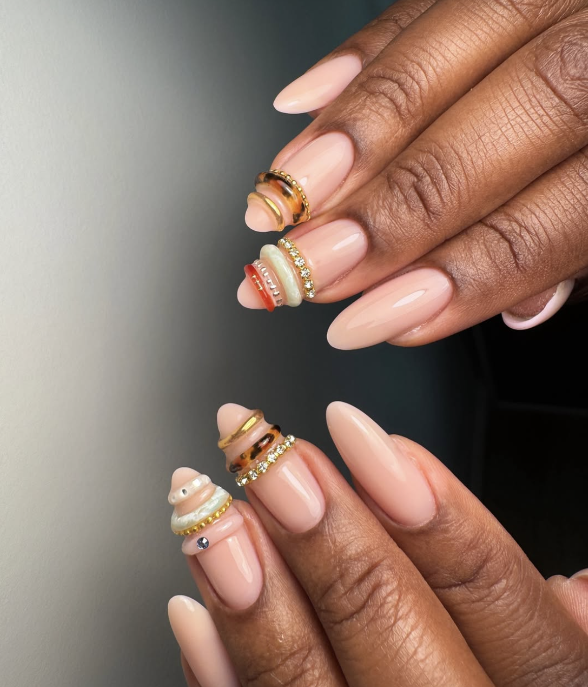 Nude and mocha almond nails featuring 3D gold wire bangles and small white pearl accents.