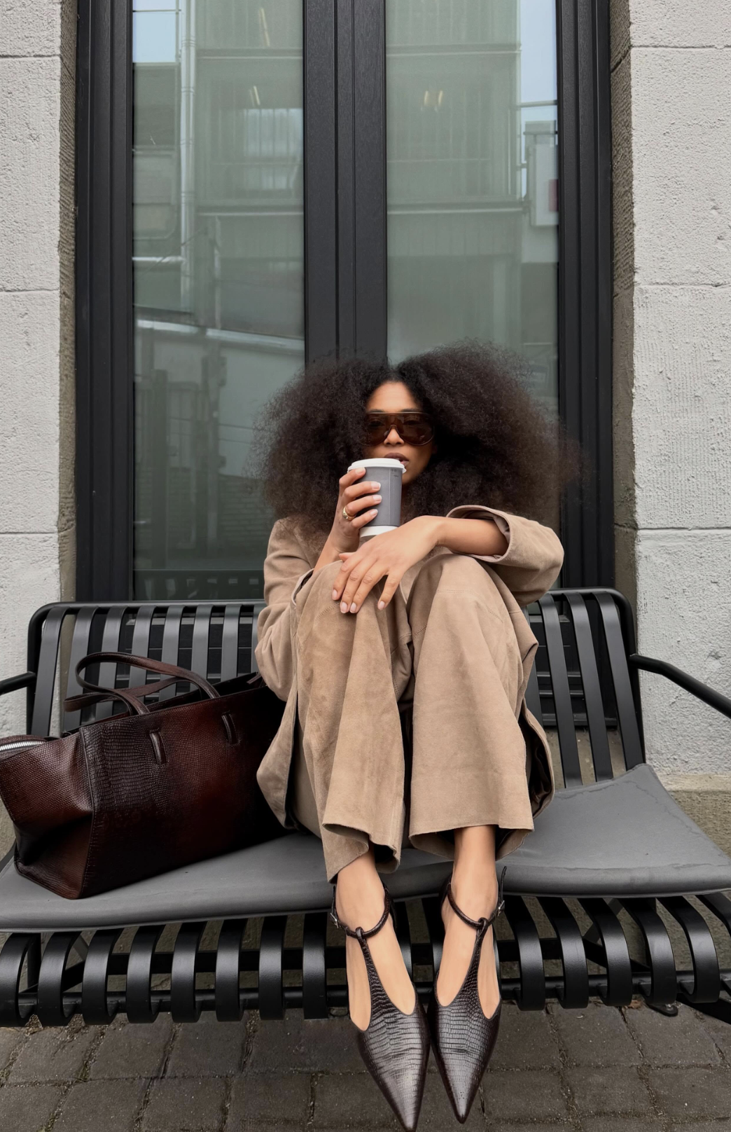 Close-up of brown textured T-strap pointed-toe flats styled with wide-leg beige trousers and a dark brown leather tote bag.