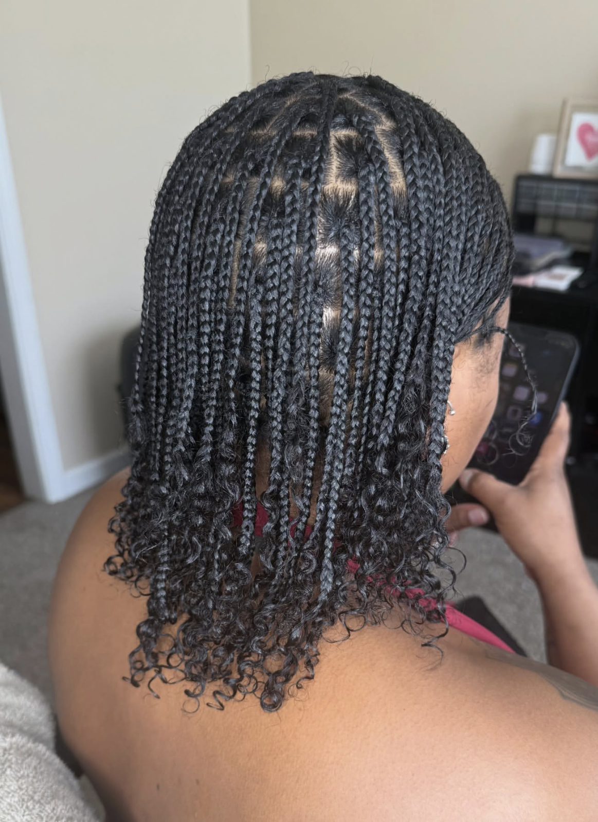 Close-up view from behind of a woman showcasing long, neat mini braids on dark natural hair with beautifully defined curly ends cascading down her back.
