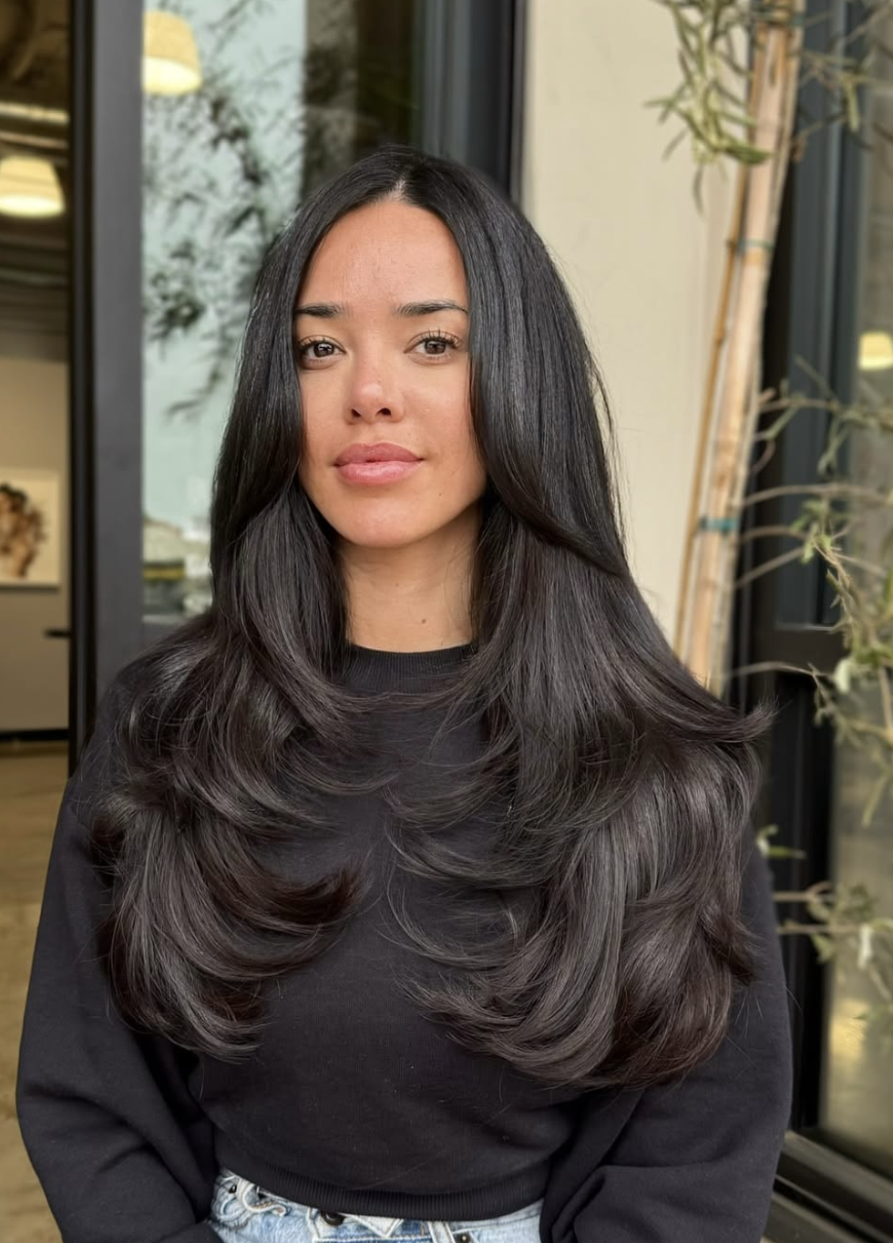 Woman with long dark hair styled in a layered butterfly haircut with bouncy face-framing layers.