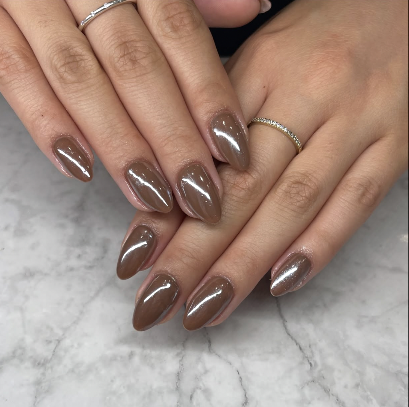 A close-up of short almond-shaped nails with a glossy, semi-sheer brown "glazed donut" chrome finish.