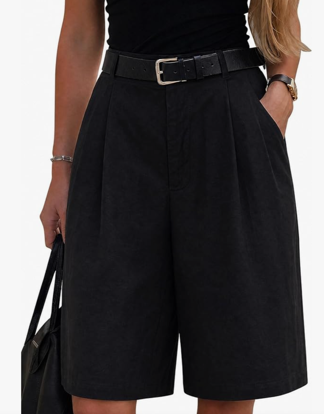 Close-up of a woman wearing high-waisted black Bermuda shorts with elegant front pleating, a matching black leather belt with a silver buckle, and holding a black leather handbag.