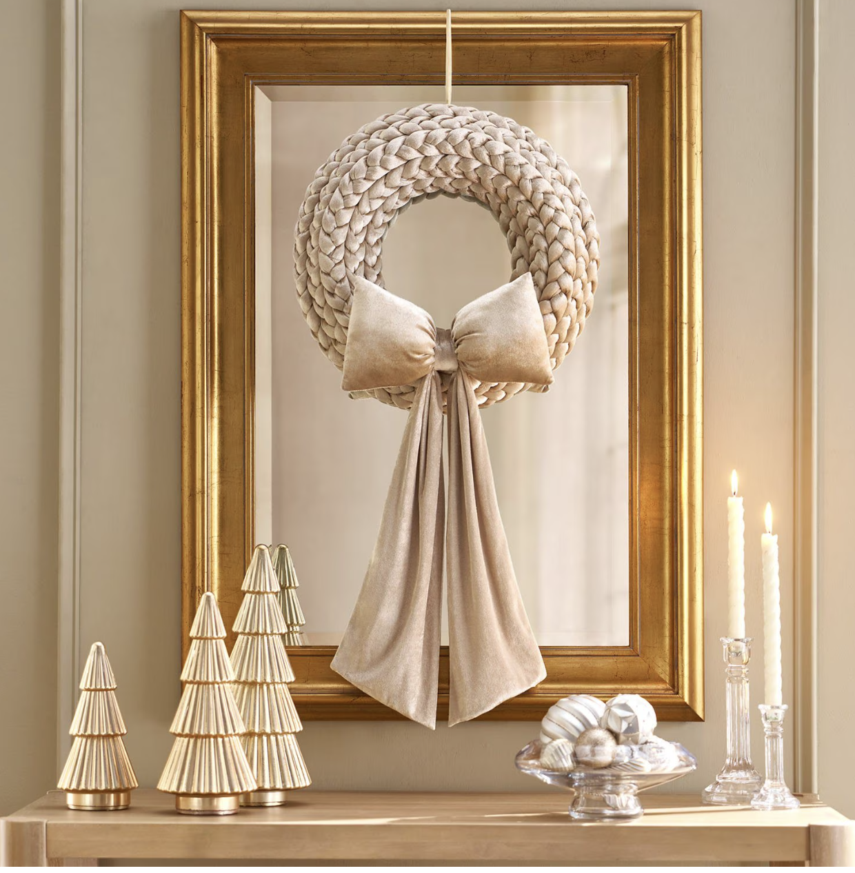 Winter-white mantel with a cream braided wreath and velvet bow on a gold mirror, gold ribbed trees and white taper candles.
