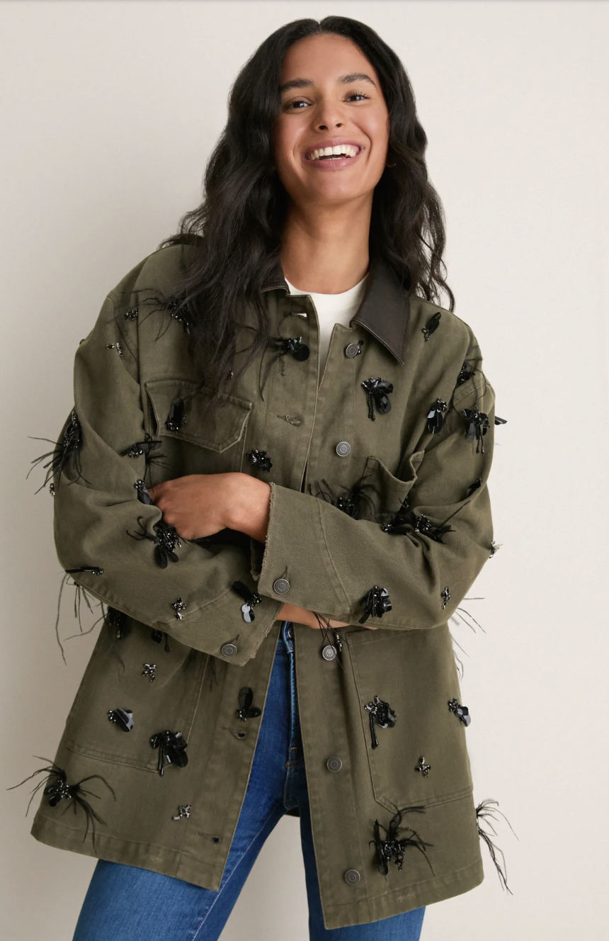 Olive green field jacket featuring embellished insect details styled over blue jeans.