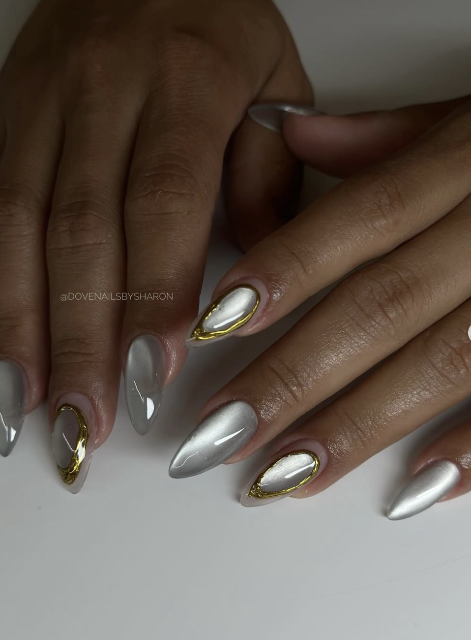 Long almond nails with a shimmering silver base and 3D gold metallic chrome borders.