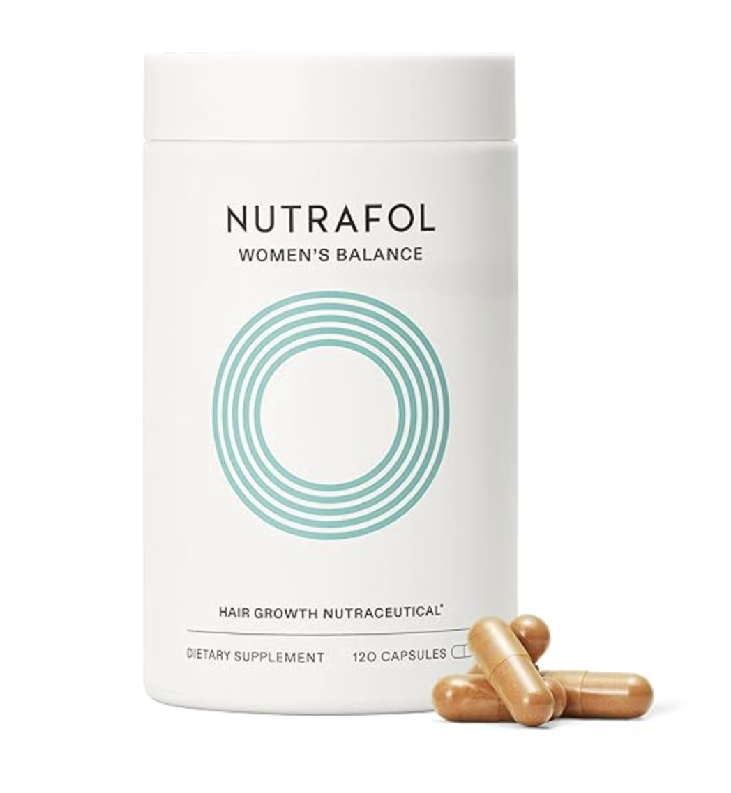 A front-facing product shot of a white bottle of Nutrafol Women's Balance Hair Growth Nutraceutical, featuring its signature teal concentric circles logo and a couple of gold capsules resting next to it.