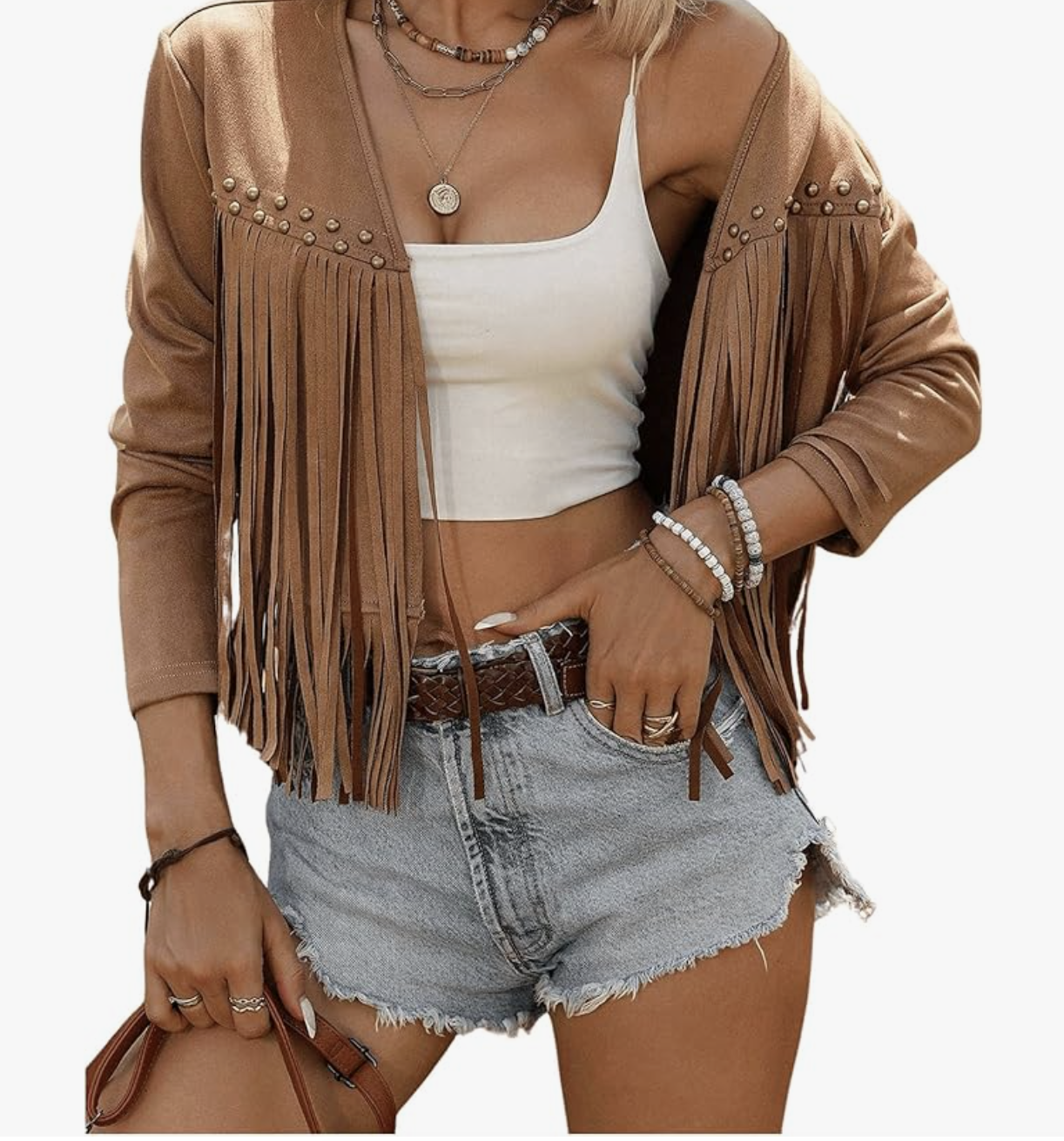 A woman wearing a white knit cardigan with long fringe tassels along the hem, styled with denim shorts and a brown leather belt.