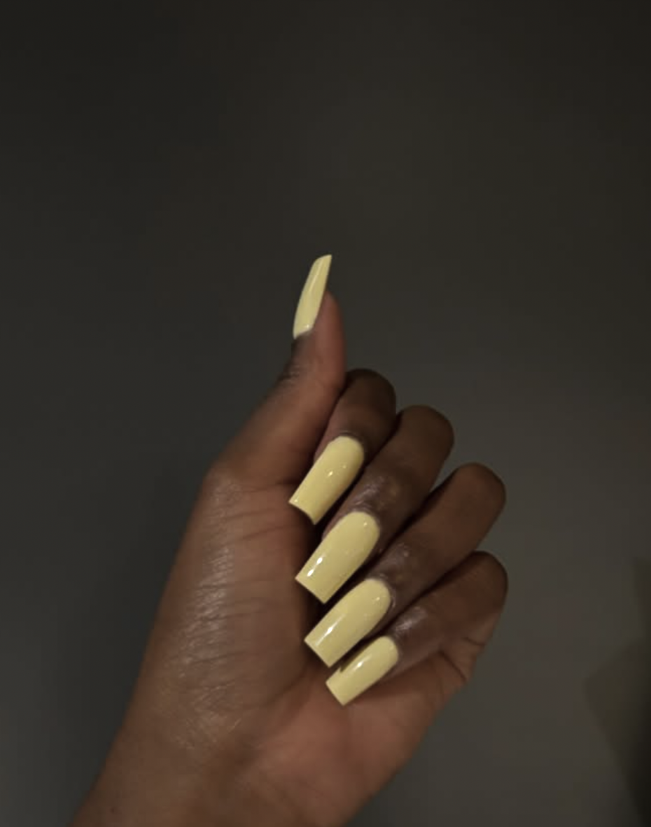 A close-up of long almond-shaped gel nails in a creamy, soft butter yellow finish.
