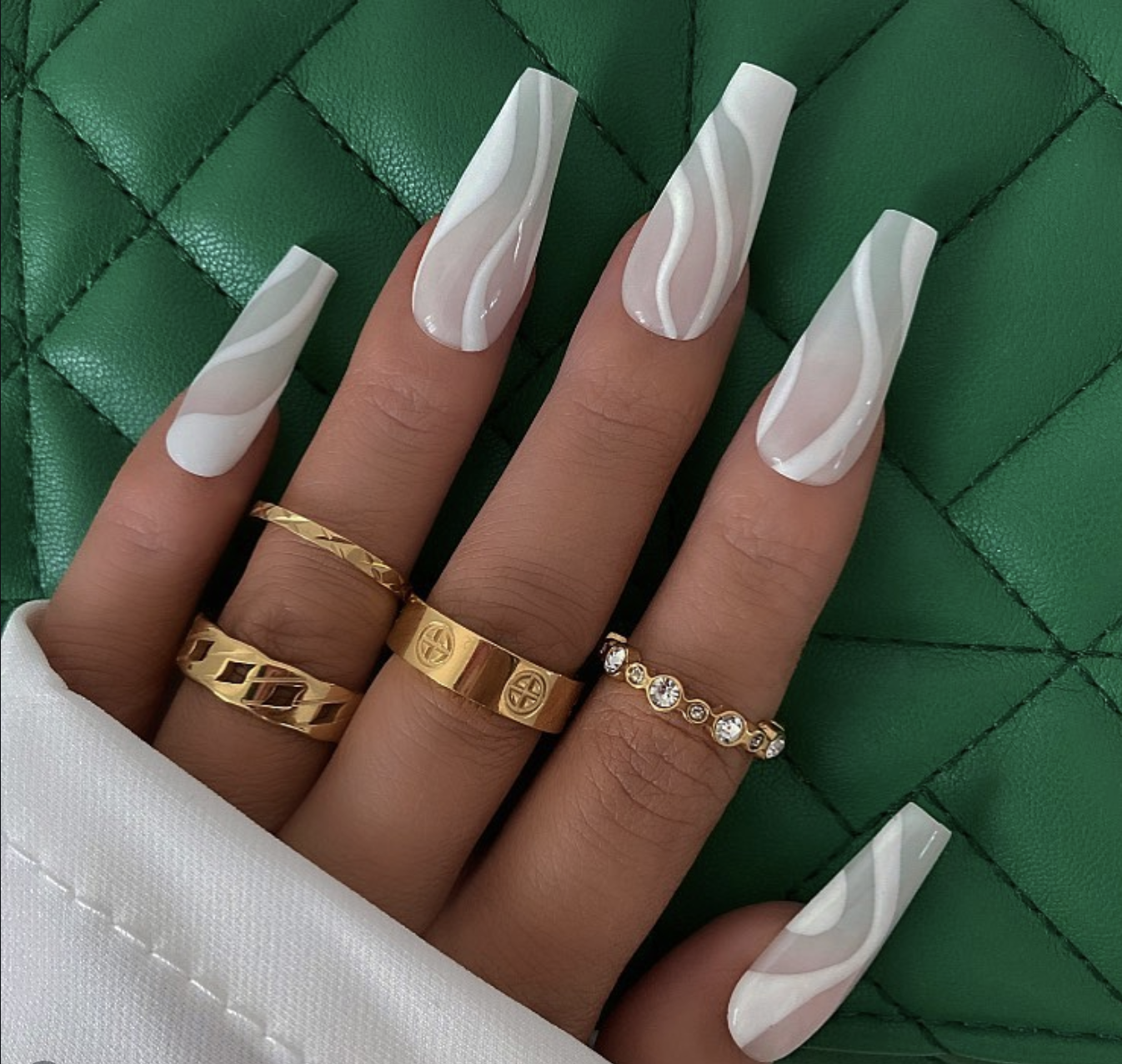 Long, coffin-shaped nails with a translucent bare base featuring bold, fluid abstract waves of opaque white polish.