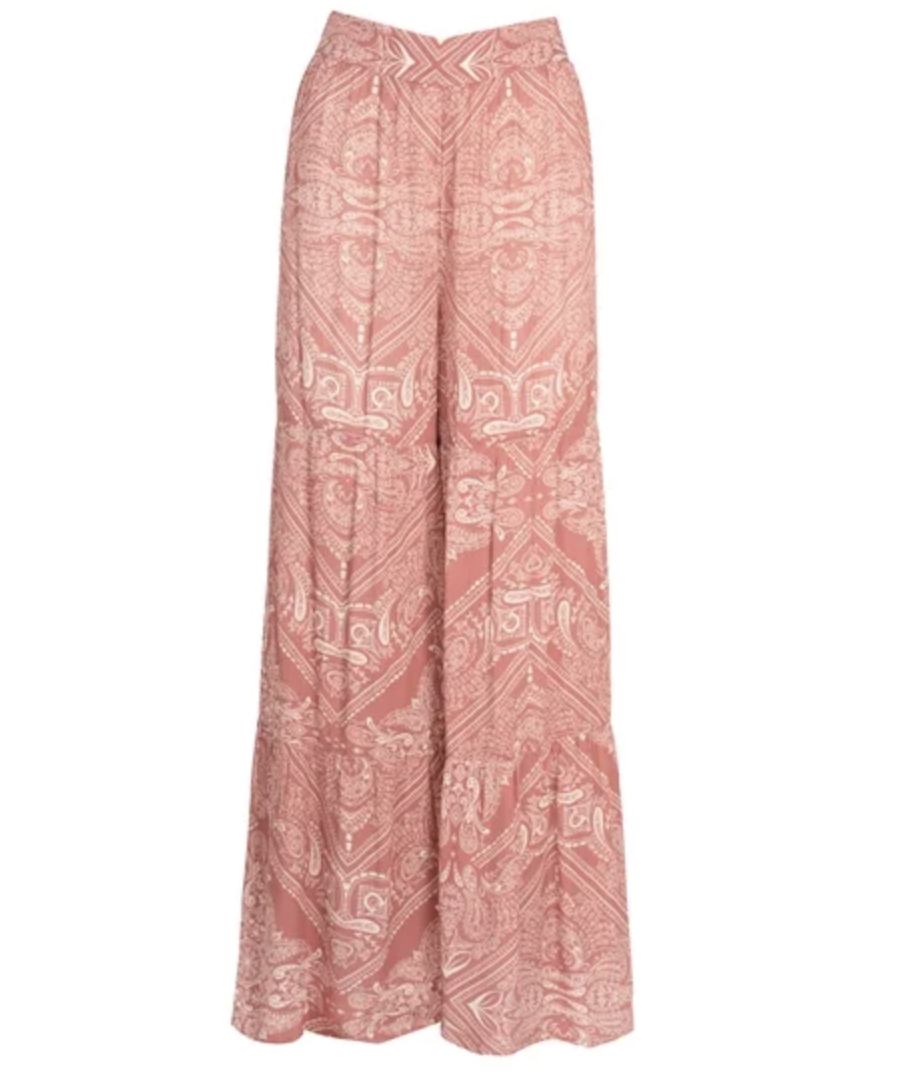 A close-up view of a pair of high-waisted, wide-leg resort pants featuring a vibrant pink and mauve paisley pattern with a tiered ruffe hem at the bottom.