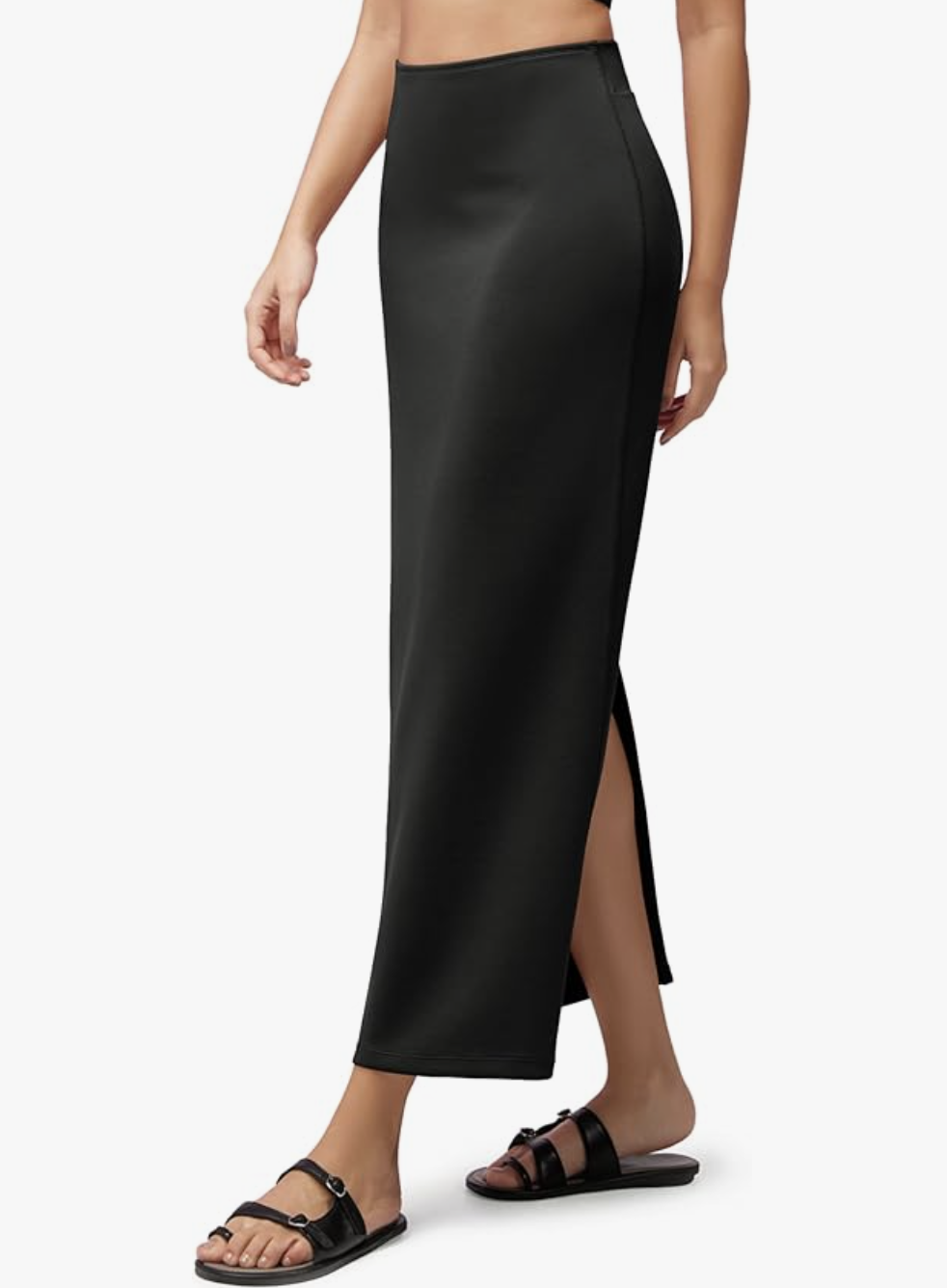 A person wearing a black ODODOS modal soft maxi skirt with a side-back slit and black strappy sandals on a white background.